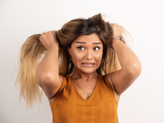 Mujer preocupada jalándose el pelo porque podría estar dañado por los procesos químicos